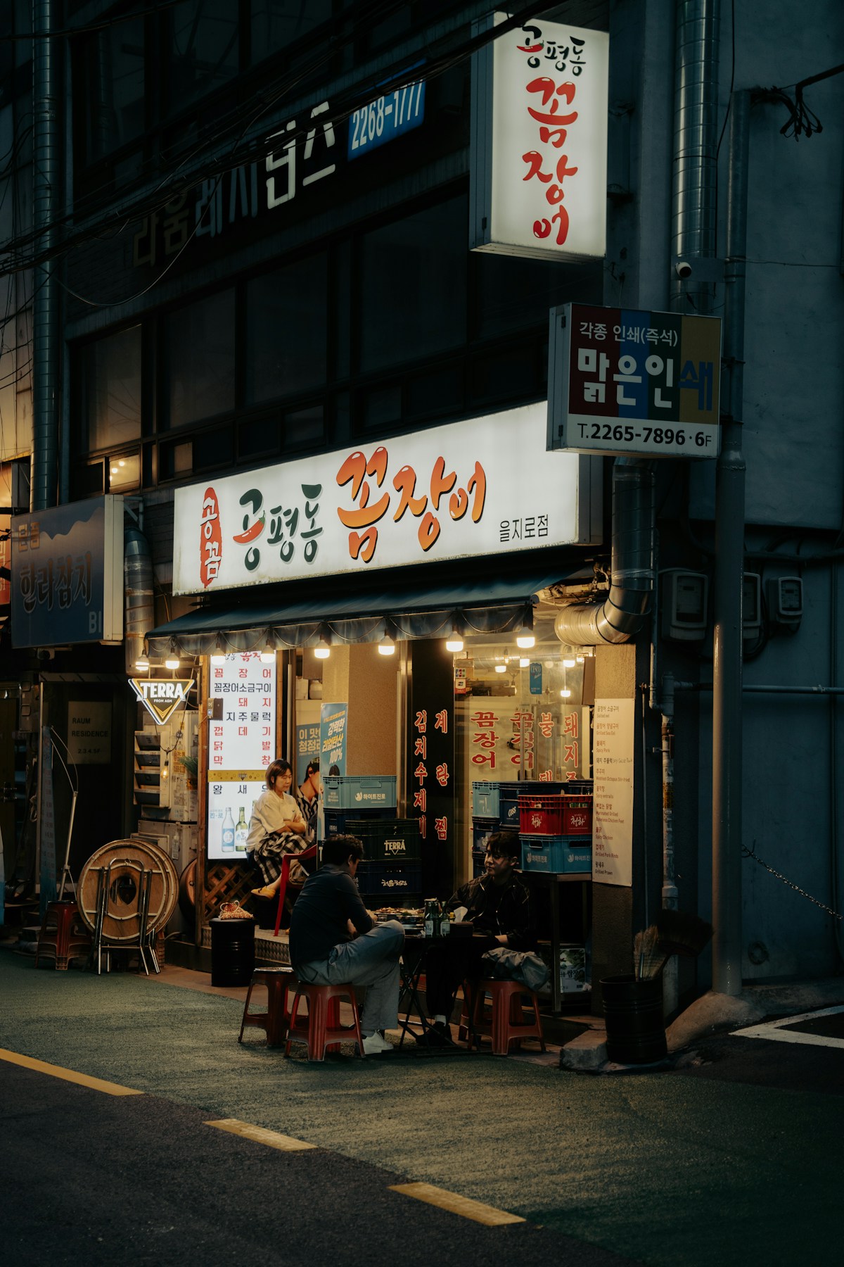 People eating outside a brightly lit Korean restaurant at night, South Korea