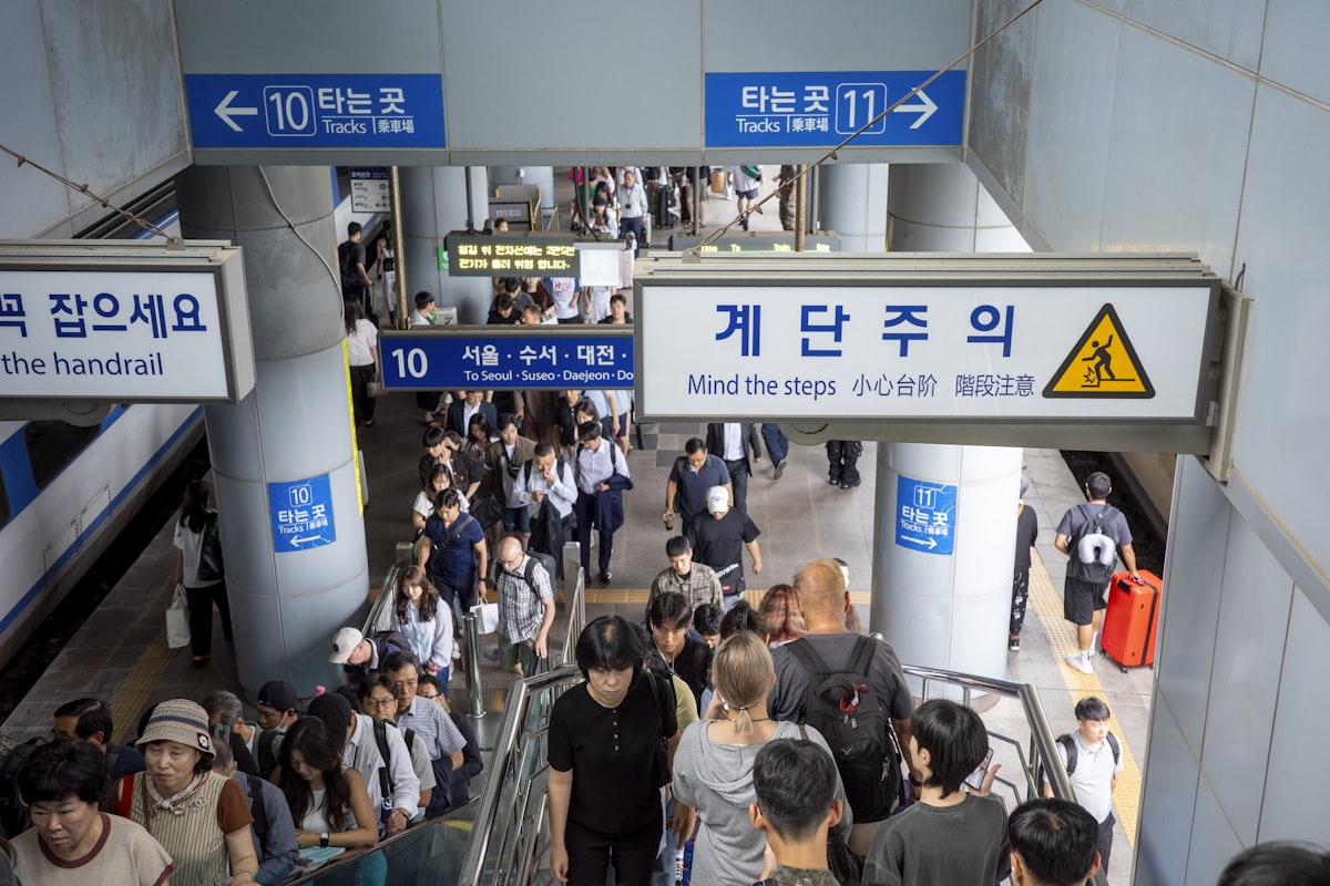 Busy Korean subway station concourse with signage in Korean, passengers on escalators