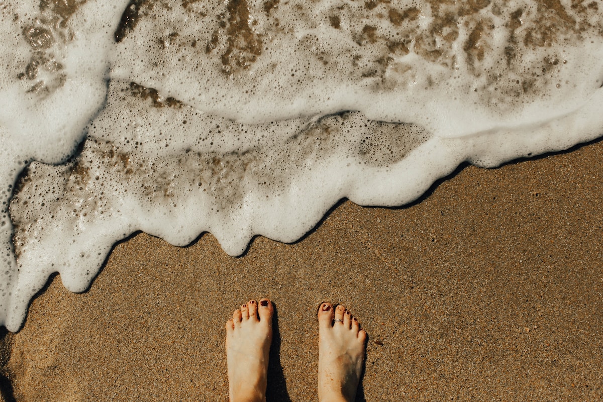 Bare feet standing at the edge of a sandy beach with ocean waves, Gangneung, South Korea