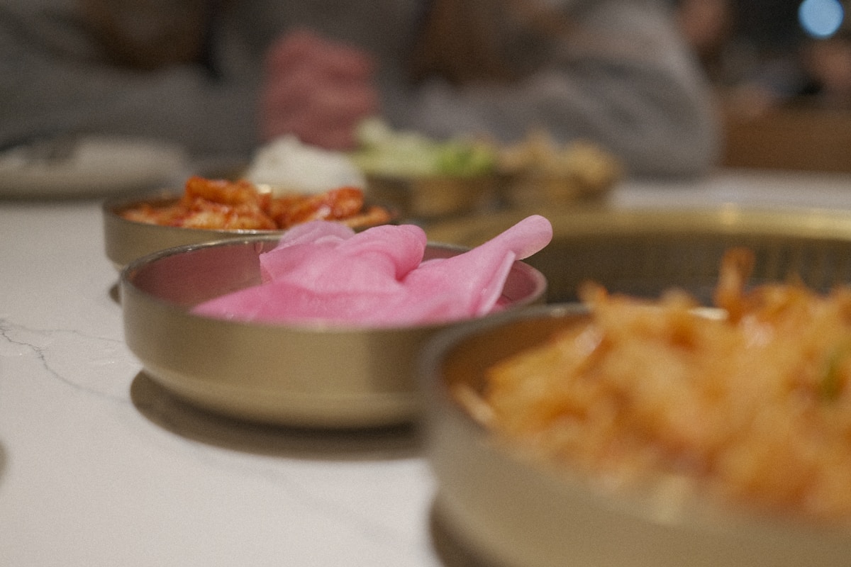 Hands preparing Korean dishes with colourful ingredients on a wooden table during a cooking class