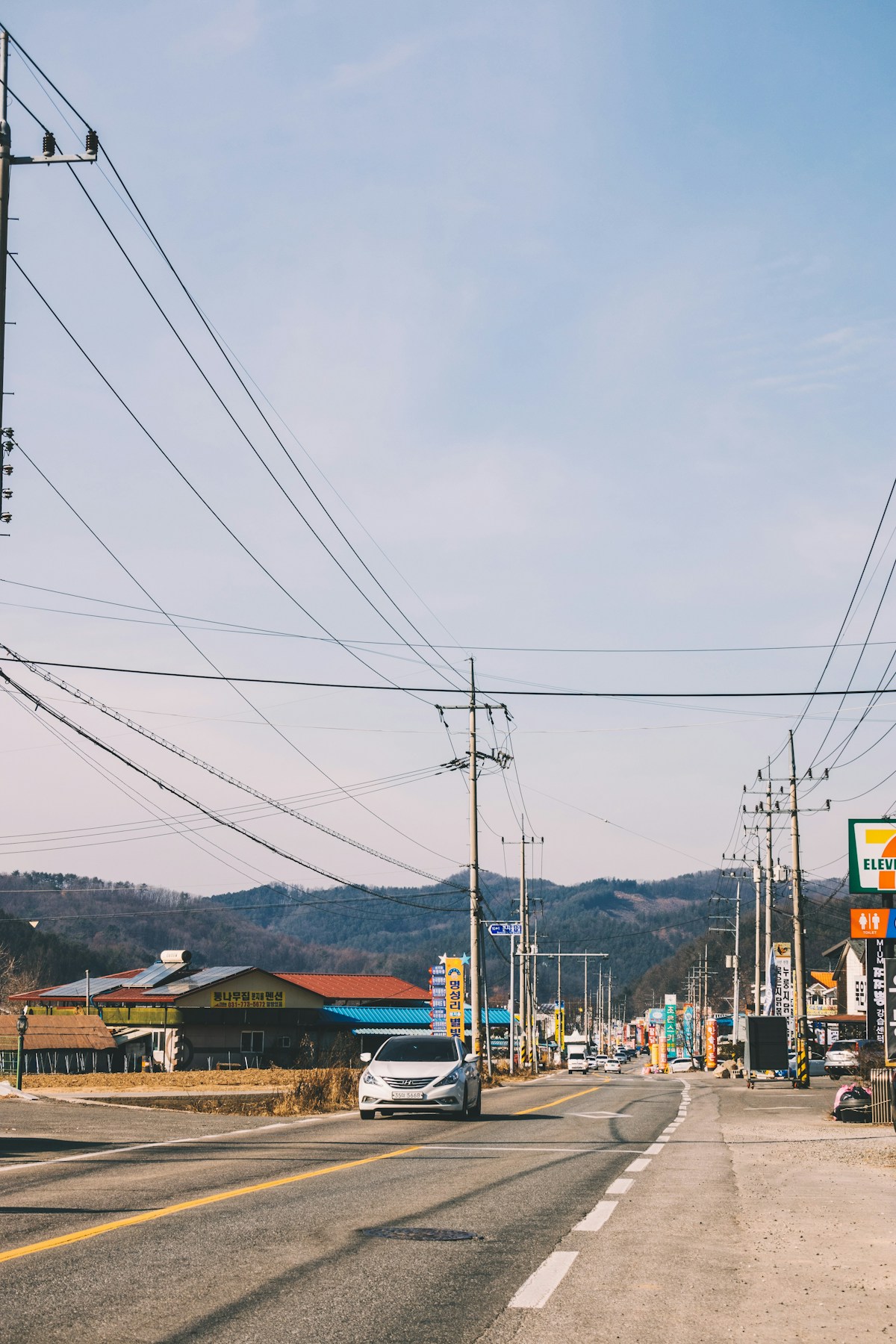 Silver car driving along a Korean road with Korean-language signs and shops, Gangwon-do, South Korea