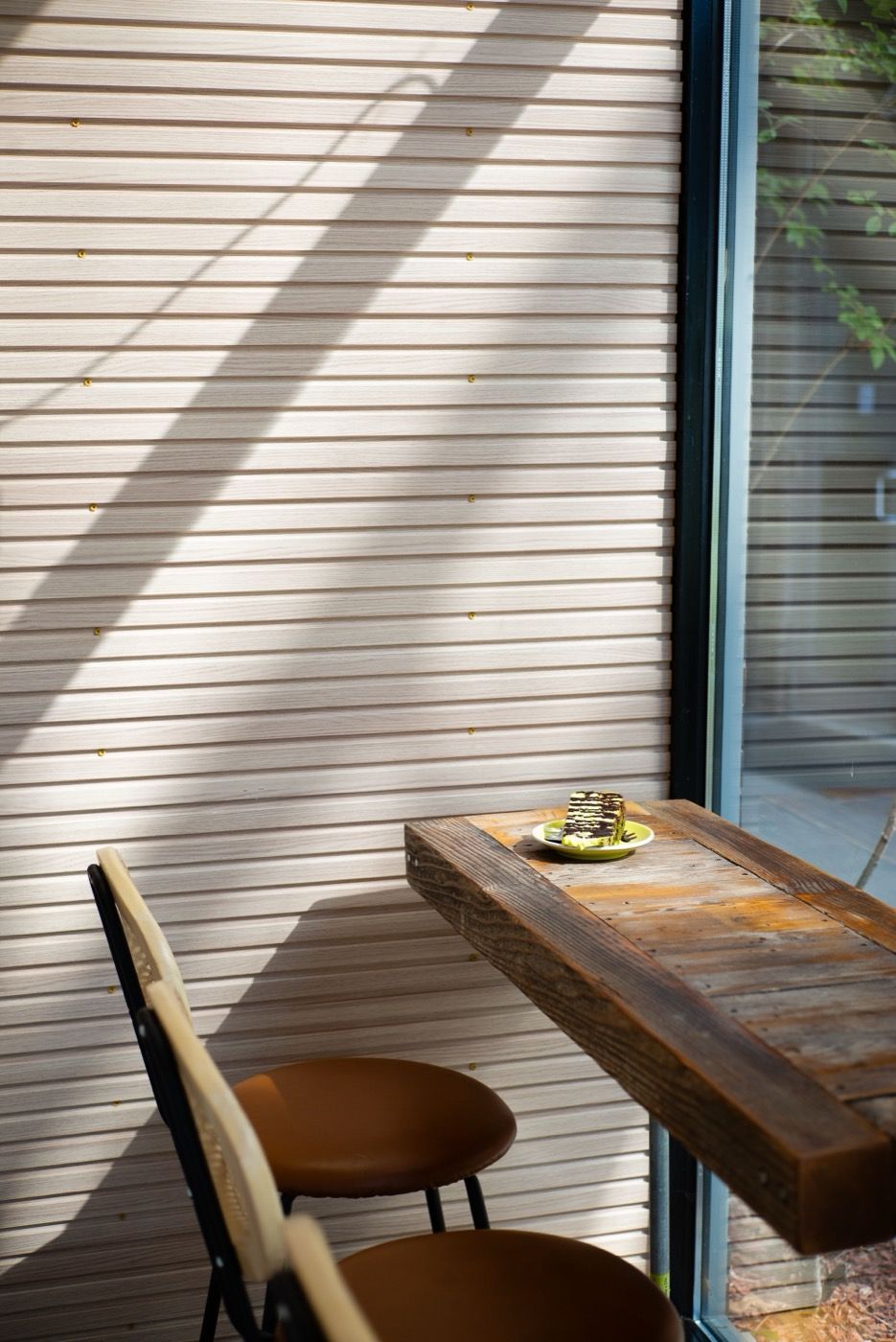 Minimalist cafe corner with sunlit wooden bench table and warm louvred wall in Seoul